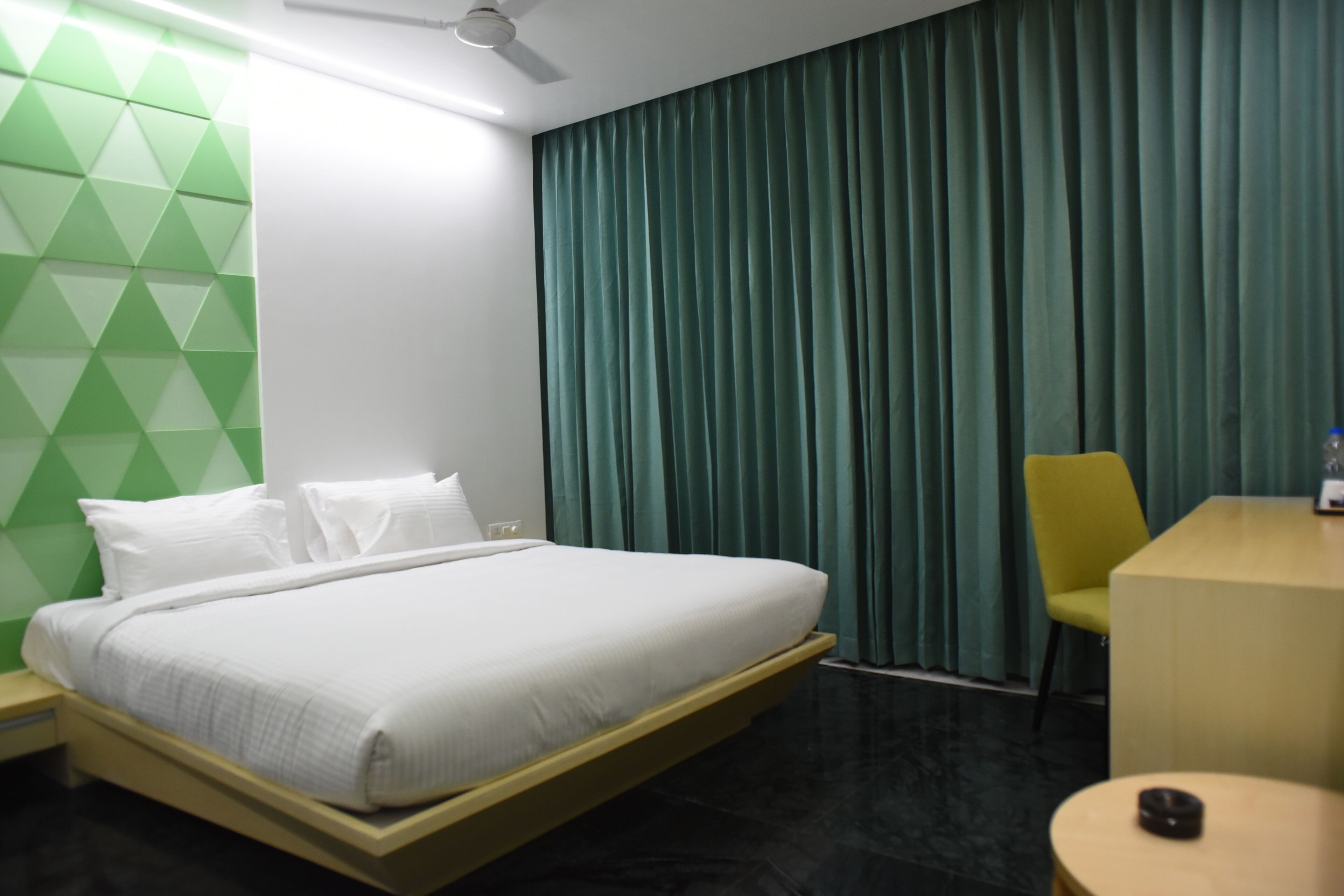 A hotel room with a bed, a desk, a chair, and a curtain.