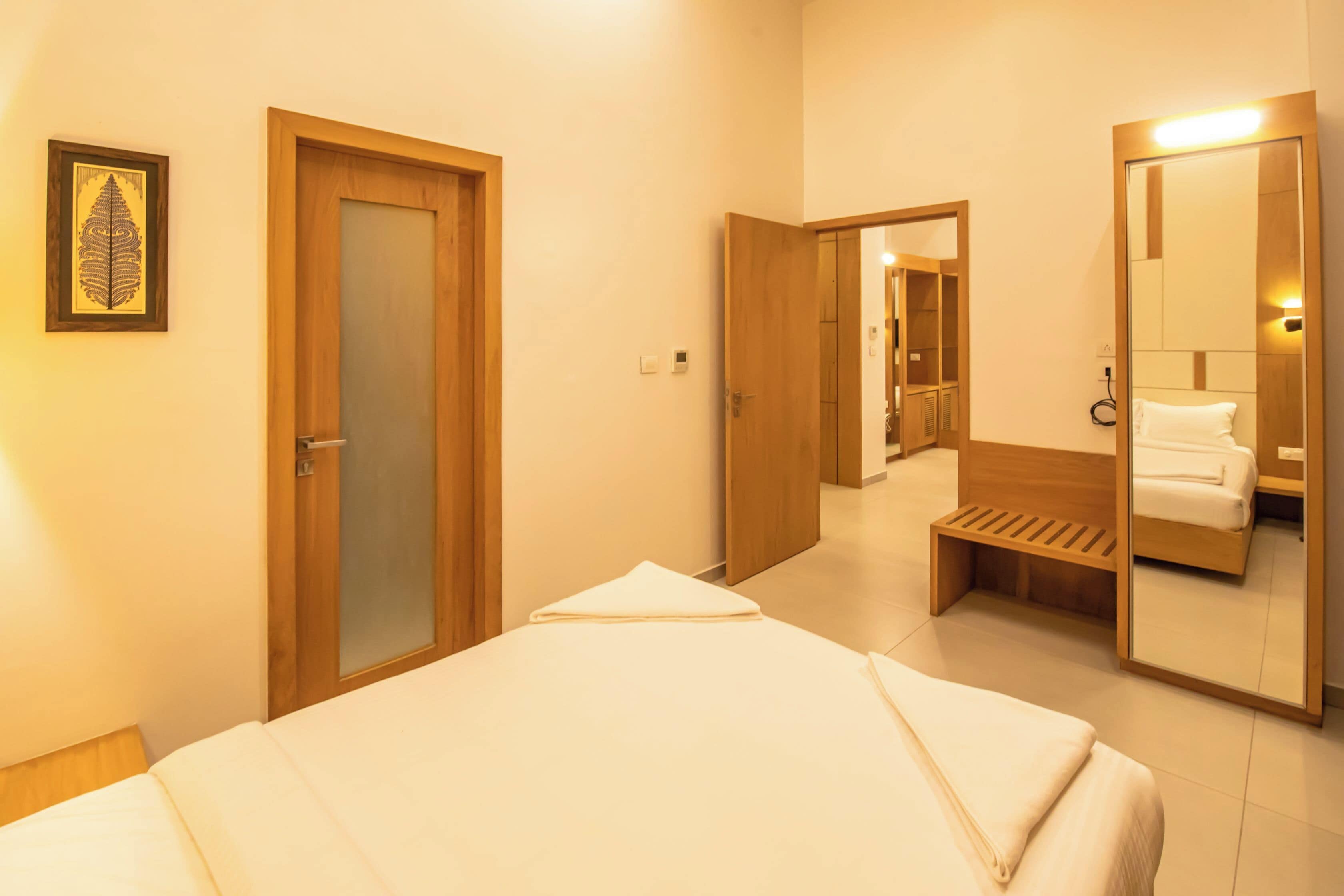 A hotel room with a bed, a bathroom with a mirror, and a door leading to another room.