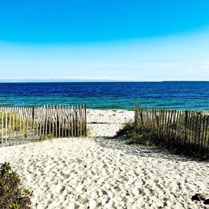 A sandy beach with a wooden fence leading to the ocean. - Modern Waterfront Home & Exclusive Quissett Beach (Falmouth)