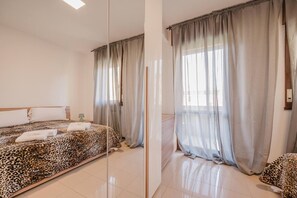 A hotel room with a bed, a nightstand, and a window with sheer curtains.