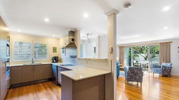 A modern kitchen with a central island, wooden flooring, and a dining area with two patterned chairs. - Seadrift 4 on Browning Street (Byron)