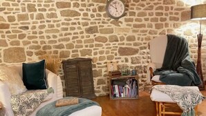 A cozy room with a stone wall, wooden furniture, and a clock. - Les Gîtes Romeline (Sartilly-Baie-Bocage)
