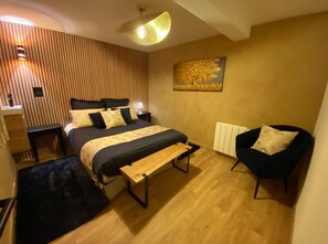 Un dormitorio moderno con cama, mesitas de noche, un banco, una silla y una obra de arte en la pared.