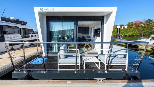 A modern houseboat with a glass facade, a dining area, and a kitchen.