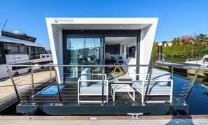 A modern houseboat with a glass facade, a dining area, and a kitchen.