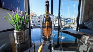 A bottle of Prosecco on a glass table with a view of boats through a window.