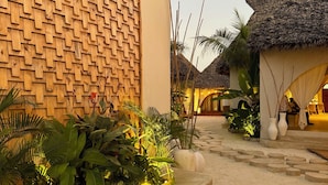 Een resort met een houten muur, rieten daken en een zandpad.