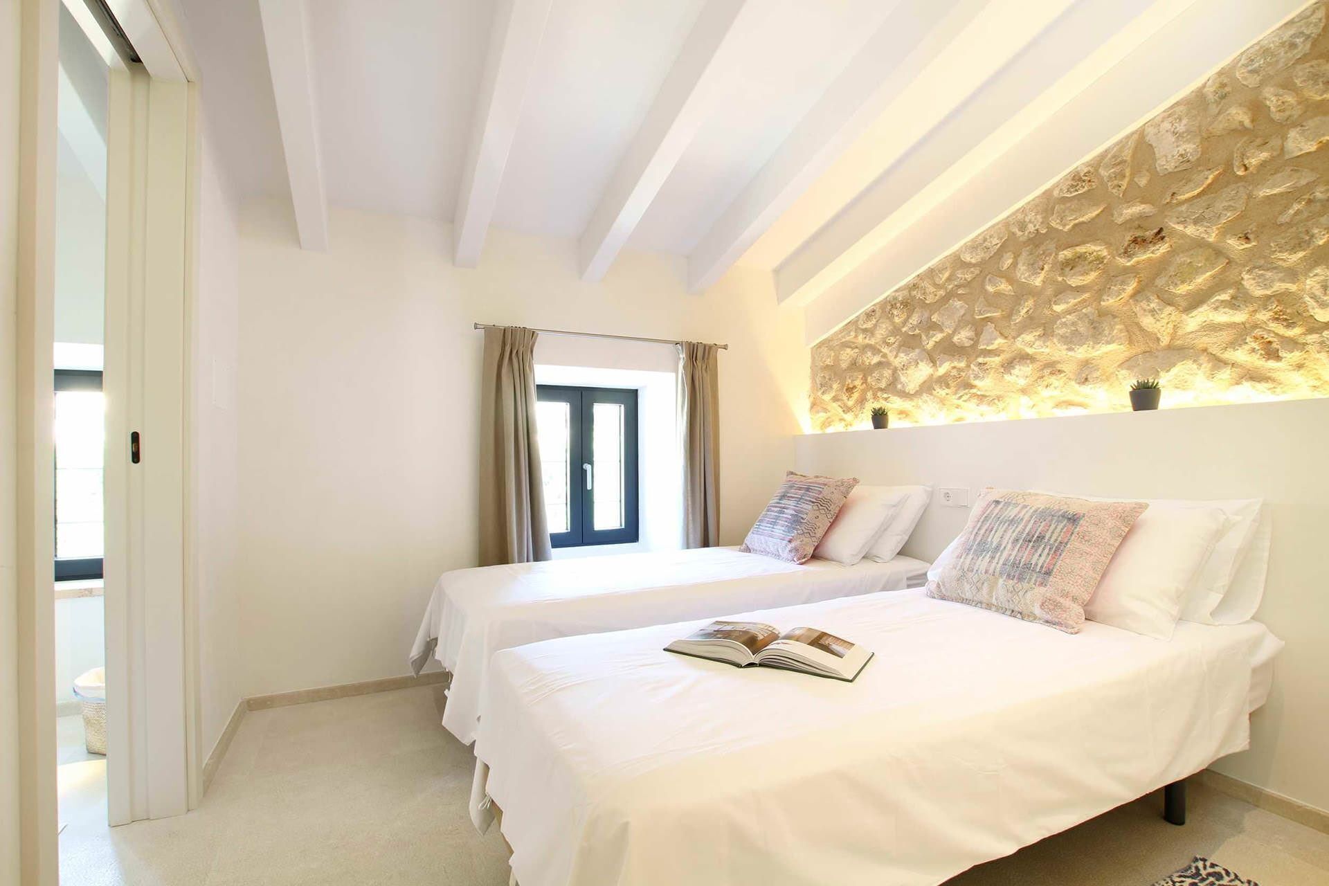 A hotel room with two beds, a stone wall, and a window with curtains.
