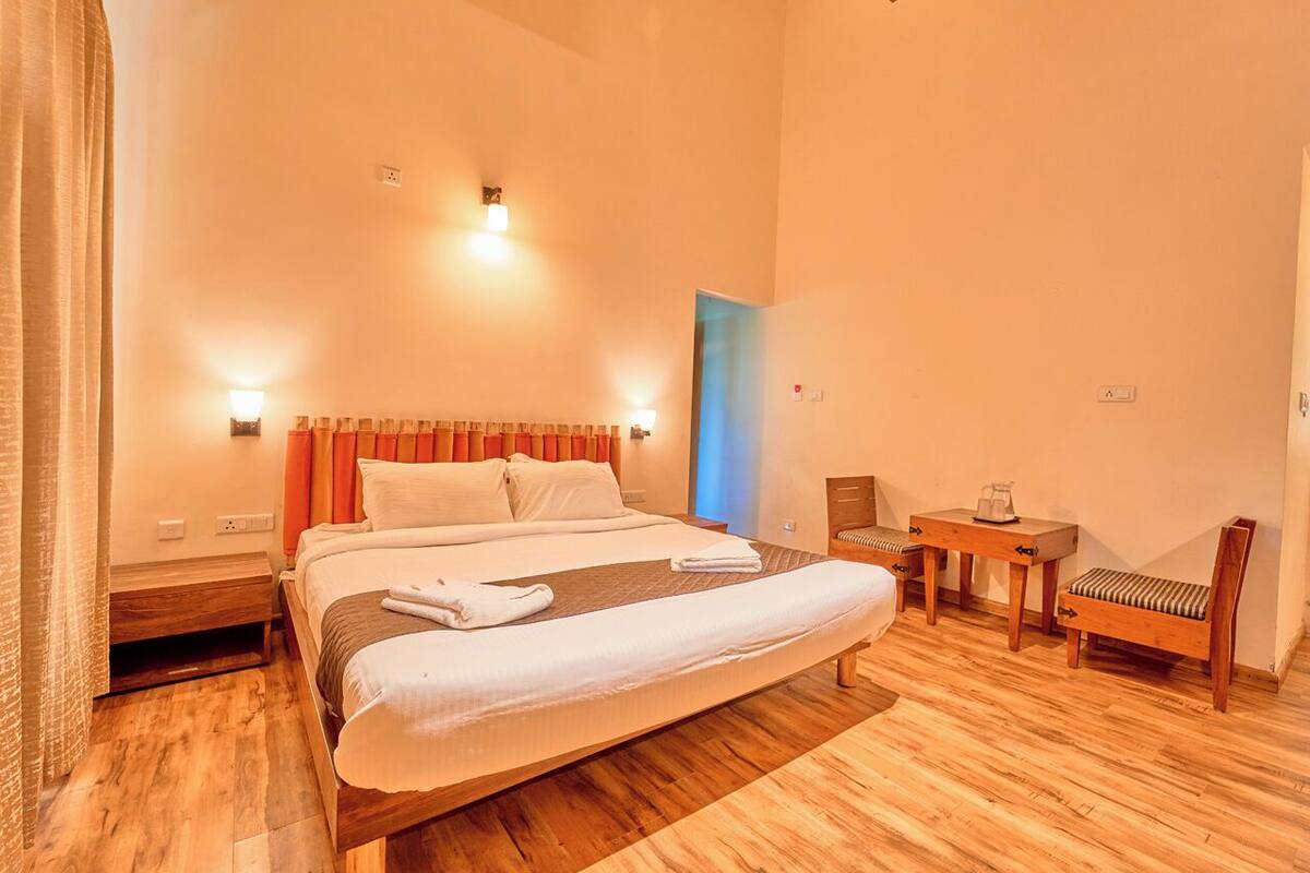 A spacious bedroom with a large bed, bedside tables, a small table with a chair, and a view of the sky through a window.