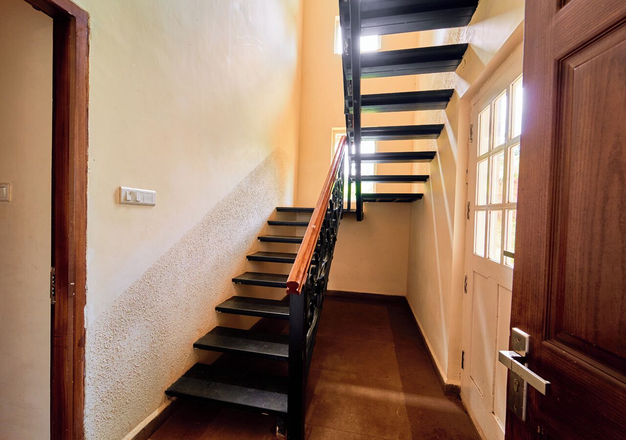 Un pasillo estrecho con una puerta de madera a la derecha y una escalera de escalones negros y barandilla de madera.
