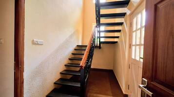 Un pasillo estrecho con una puerta de madera a la derecha y una escalera de escalones negros y barandilla de madera.