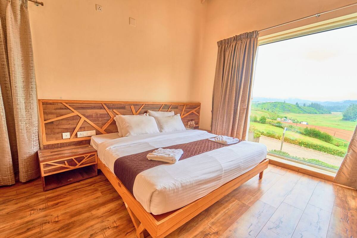 A bedroom with a wooden bed, a nightstand, and a large window with a view of a green landscape.