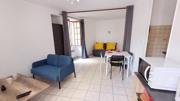 A compact living space with a blue sofa, a dining table with chairs, a kitchen area with a microwave, and a small table with a remote control. - Le Coin du Palan Chateauroux Hyper Centre (Chateauroux)