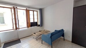 A room with a blue sofa, a wooden table, a TV, and a window with curtains. - Le Coin du Palan Chateauroux Hyper Centre (Chateauroux)