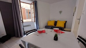 A small, modern room with a white table, red and clear glasses, a black potted plant, and a grey sofa with yellow cushions. - Le Coin du Palan Chateauroux Hyper Centre (Chateauroux)