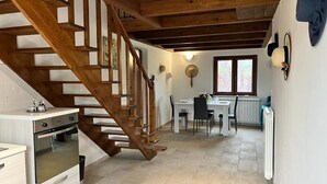 Una cocina con escalera de madera, un comedor con mesa y sillas, y un ventanal con persianas.