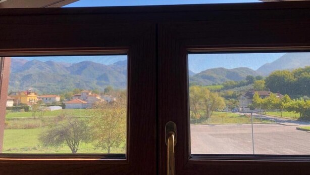 Vista a través de una puerta de madera con manija metálica, mostrando un paisaje con montañas y una carretera.
