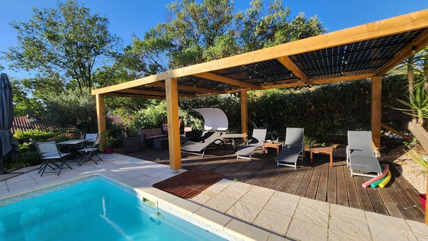 En trädgård med en pool, ett trädäck, solstolar och en pergola med solpaneler.