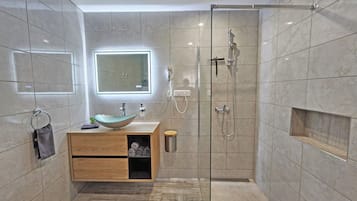 Une salle de bain moderne dotée d’une douche à parois de verre, d’un meuble-lavabo en bois avec un lavabo en forme de coupe et d’un grand miroir au-dessus du lavabo.