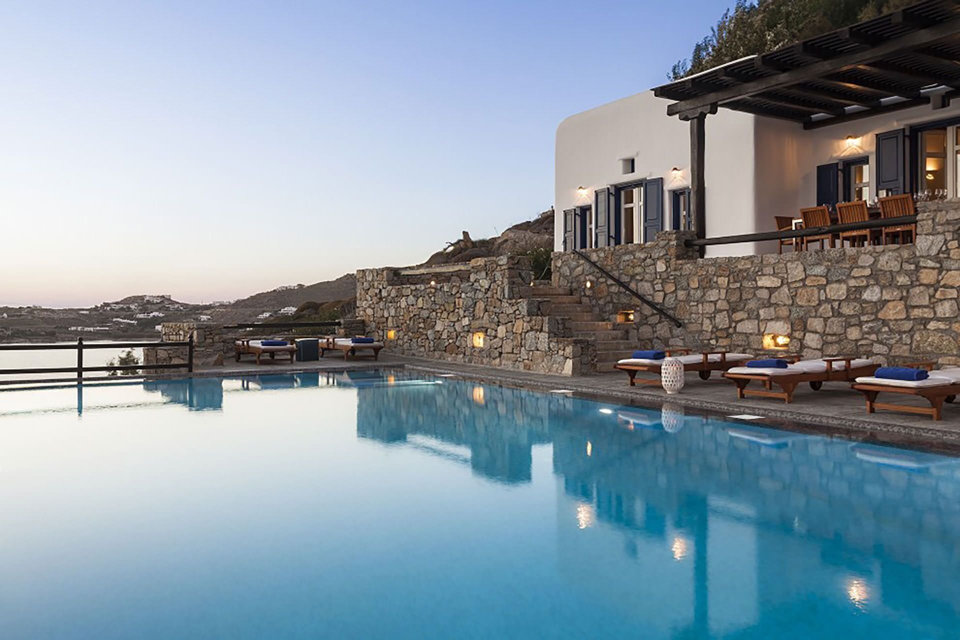 A pool area with lounge chairs, stone walls, and a view of the landscape.