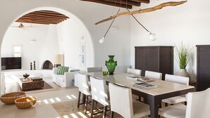 Uma sala de estar ampla, com uma mesa de jantar, sofás brancos e teto de madeira.