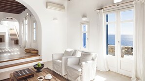 Um interior claro e branco com vista para o mar através de amplas janelas.