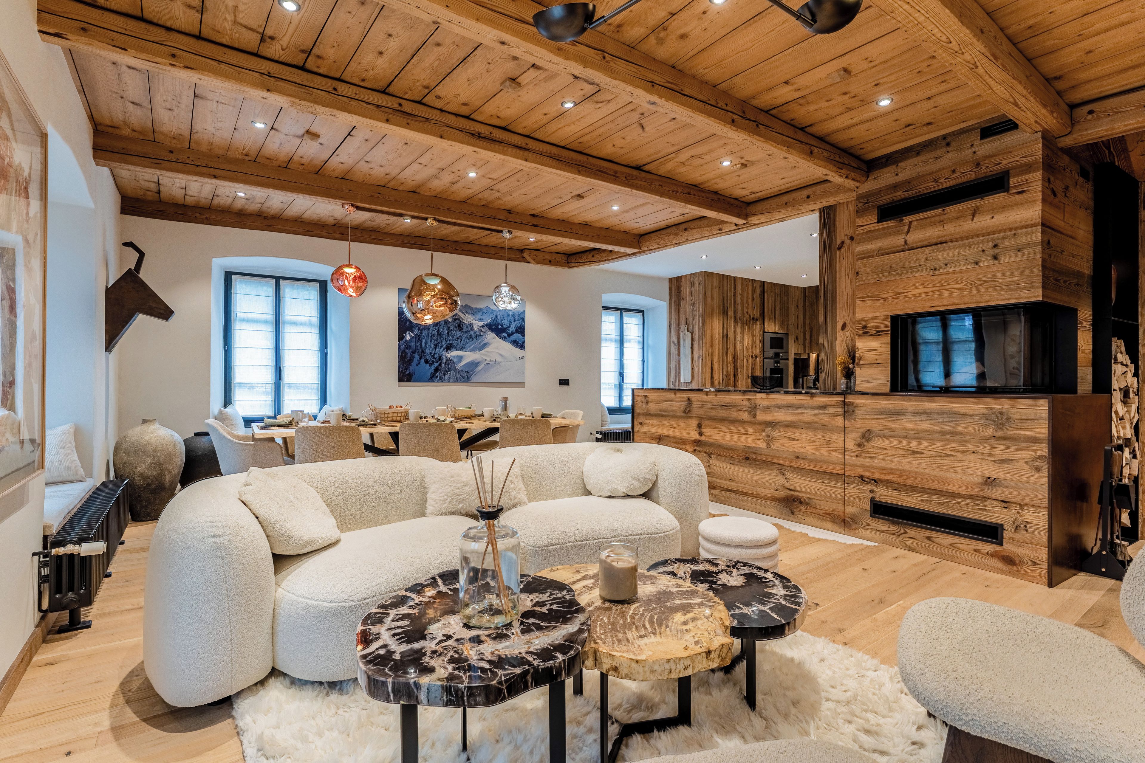 A modern living room with a wooden ceiling, a large sofa, a dining area, and a fireplace.