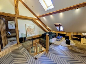 Een ruime loft met een visgraatvloer, een glazen trap en een gezellige zithoek met een bank en salontafel.