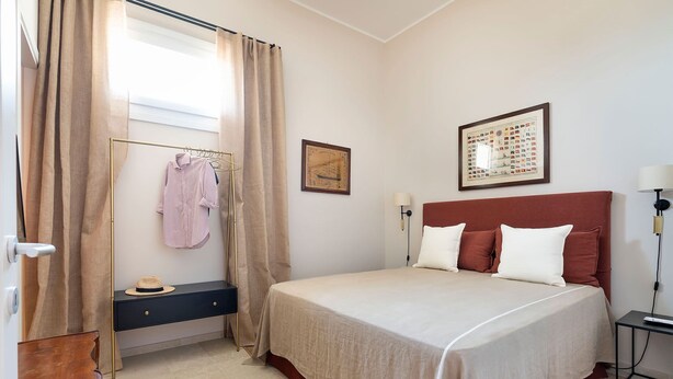 Une chambre à coucher avec un lit, une table de chevet, une lampe fixée au mur et une fenêtre avec des rideaux.