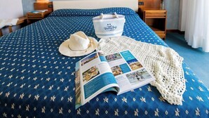 A neatly made bed with a blue patterned bedspread, a white crocheted blanket, a hat, and a magazine. - Hotel Esplanade (Cesenatico)