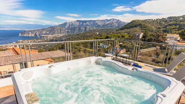 A hot tub with a mountain view, a balcony with chairs, and a clear sky. - Villa Rosa: jacuzzi with Sorrento coast view (Massa Lubrense)