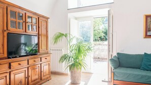 A spacious living room with a wooden entertainment unit, a large potted plant, and a green sofa. - Villa Rosa: jacuzzi with Sorrento coast view (Massa Lubrense)