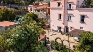 A pink villa with a stone courtyard, outdoor seating, and a view of surrounding buildings. - Villa Rosa: jacuzzi with Sorrento coast view (Massa Lubrense)