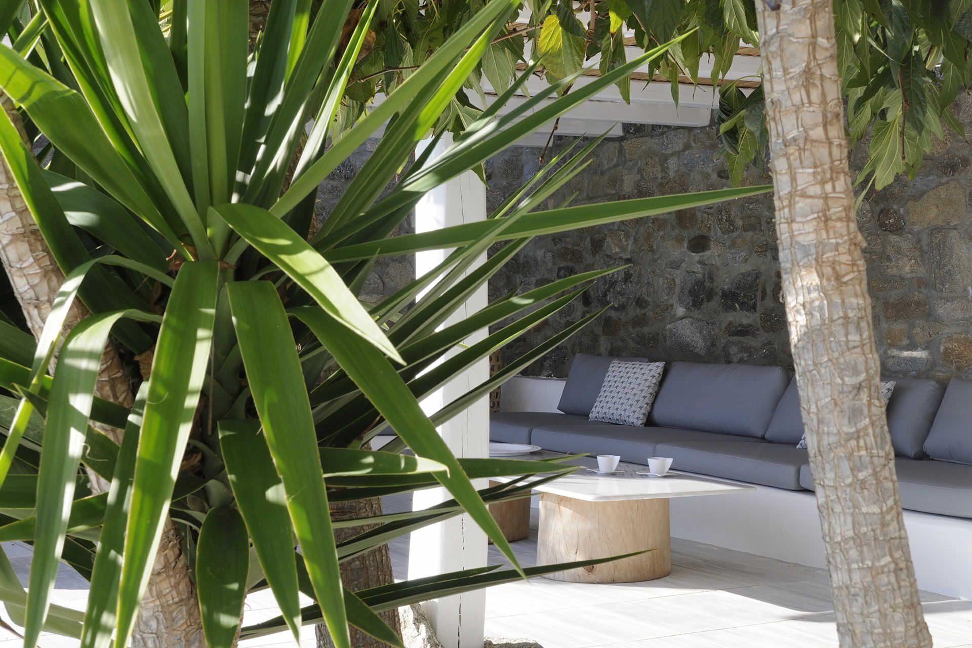 A modern outdoor seating area with a stone wall backdrop, a wooden coffee table, and a sofa with cushions.