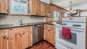A kitchen with wooden cabinets, a stainless steel dishwasher, a white stove, and a chandelier. - Stonehenge  Tobermory - Rustic Waterfront Retreat (Tobermory)