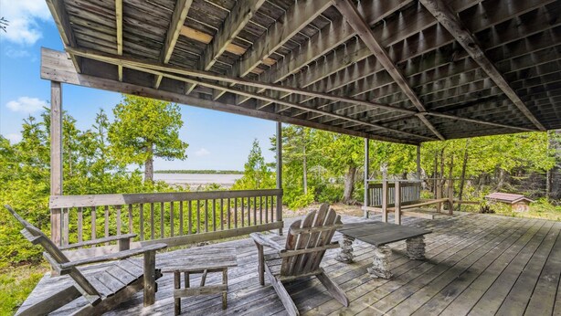 A wooden deck with a covered area, outdoor seating, and a view of a body of water. - Stonehenge  Tobermory - Rustic Waterfront Retreat (Tobermory)