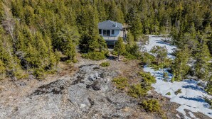 A remote cabin surrounded by dense forest, with a rocky ground and patches of snow. - Stonehenge  Tobermory - Rustic Waterfront Retreat (Tobermory)