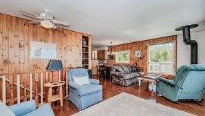 A cozy living room with a blue armchair, a sofa, a fireplace, and a dining area with a table and chairs. - Stonehenge  Tobermory - Rustic Waterfront Retreat (Tobermory)