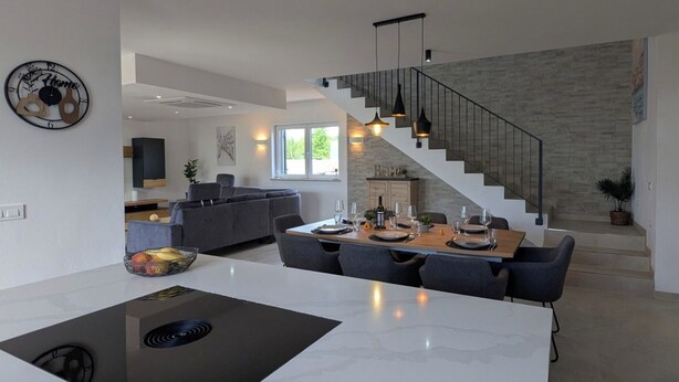 A modern kitchen with a central island, a dining area with a wooden table and chairs, and a staircase leading to an upper level. - Villa for 8 people in Višnjan near Poreč (Višnjan)