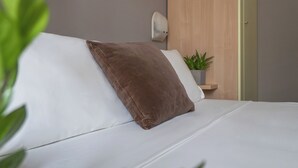 A modern bedroom with a bed, a nightstand, a wall-mounted lamp, and a small potted plant. - Vibe Hotel (Cattolica)