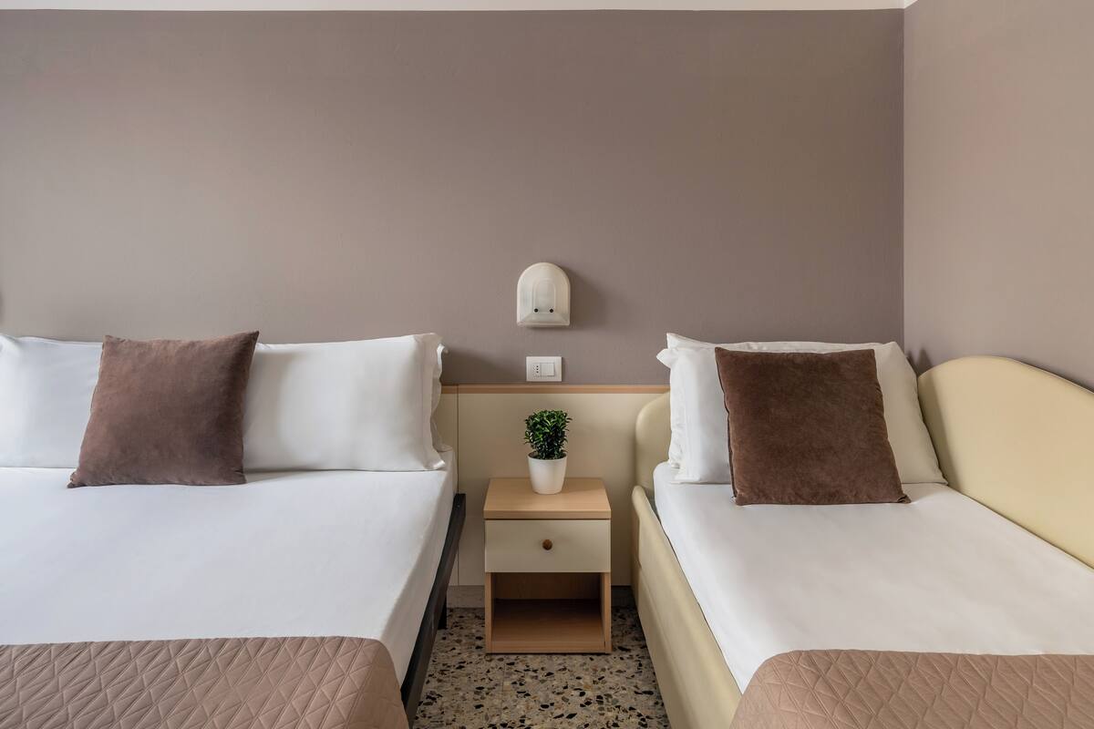 A hotel room with two beds, a nightstand with a plant, and a wall-mounted light fixture.