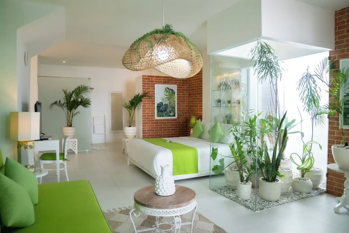 Een moderne slaapkamer met een groen bed, witte meubels en een grote spiegel. Er staan potplanten en er hangt een lamp.