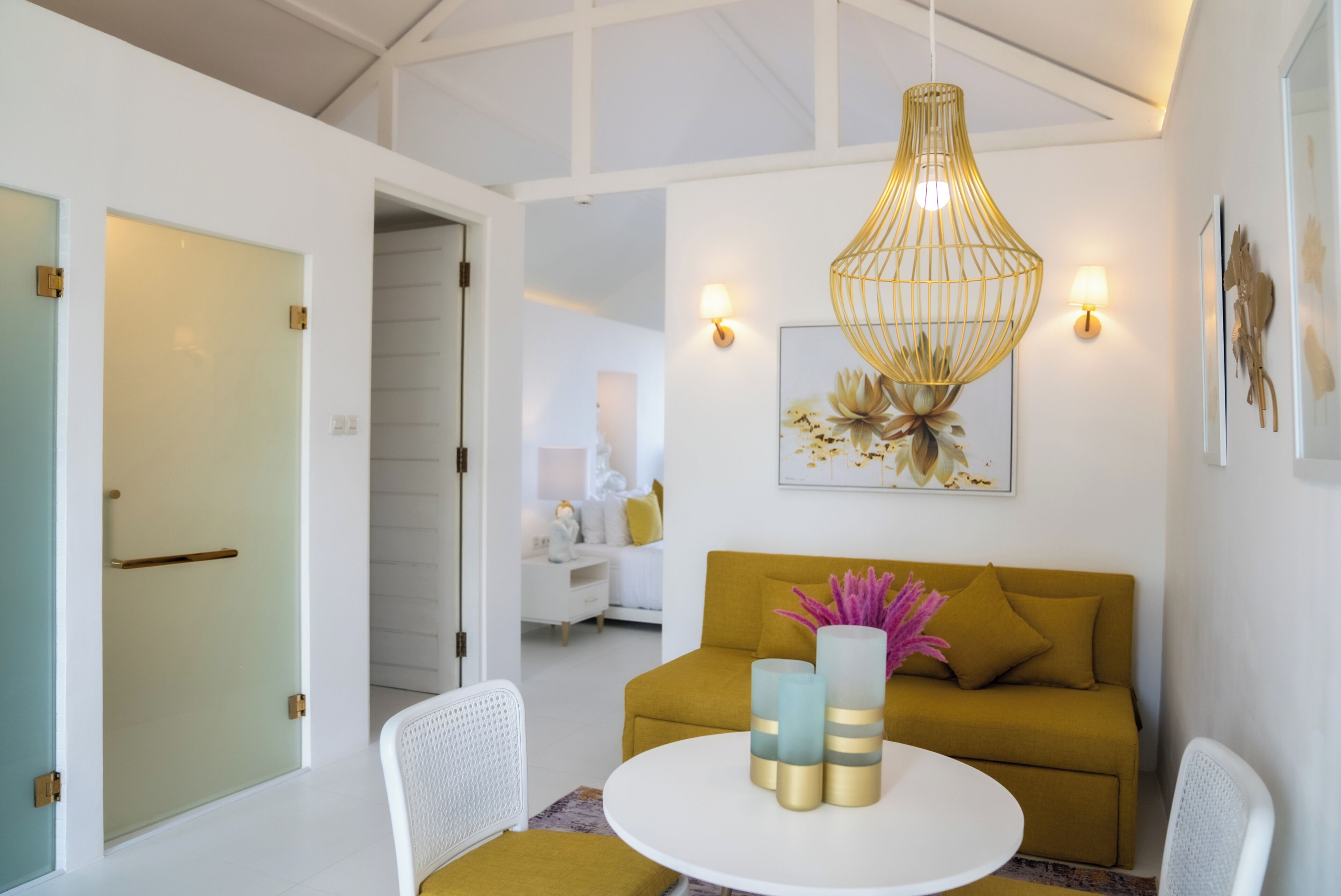 Ein modernes Wohnzimmer mit einem runden weißen Tisch, einem senfgelben Sofa und einer einzigartigen goldfarbenen Pendelleuchte.