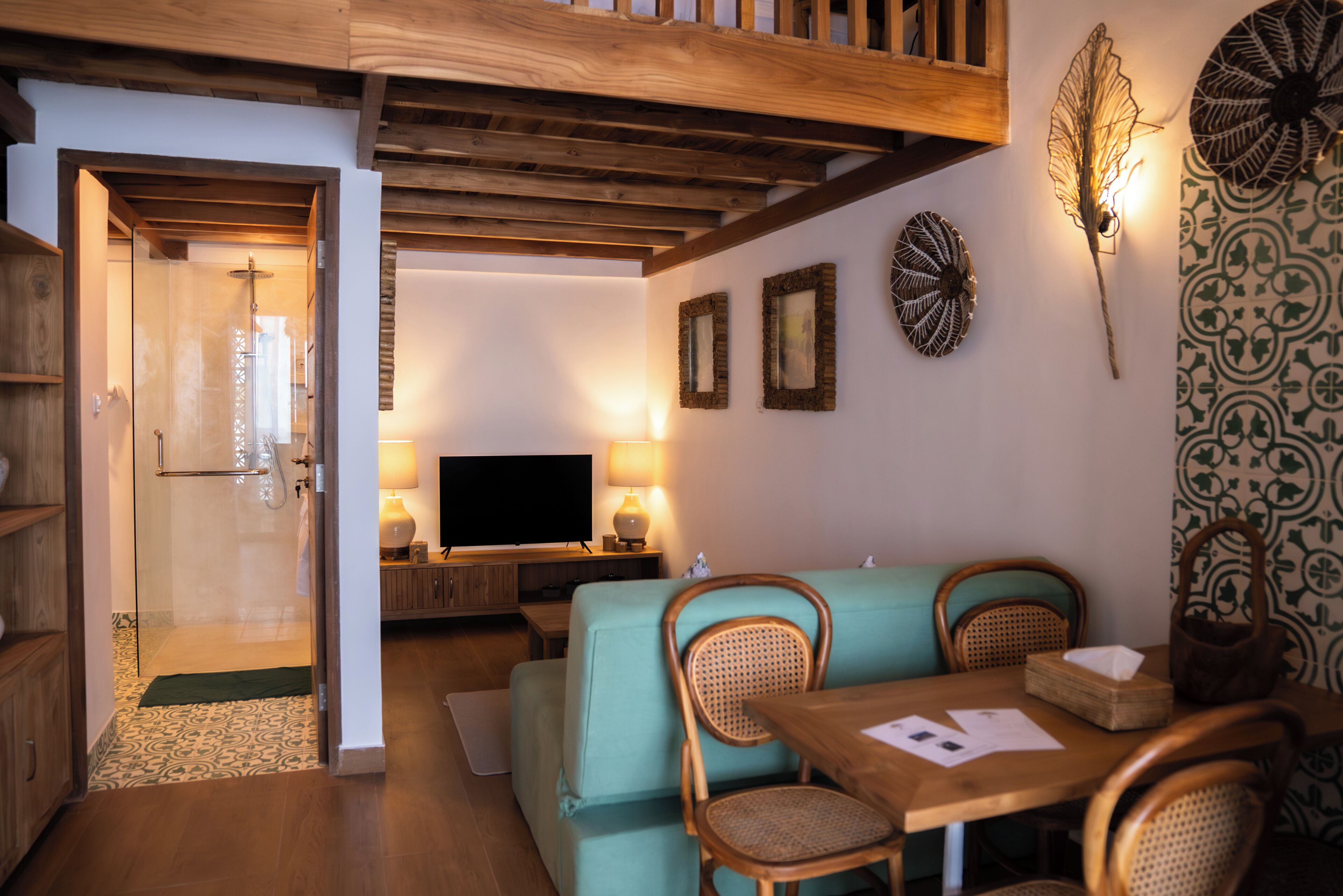 A cozy living room with a sofa, wooden table, and chairs. There is a television and a decorative wall piece.