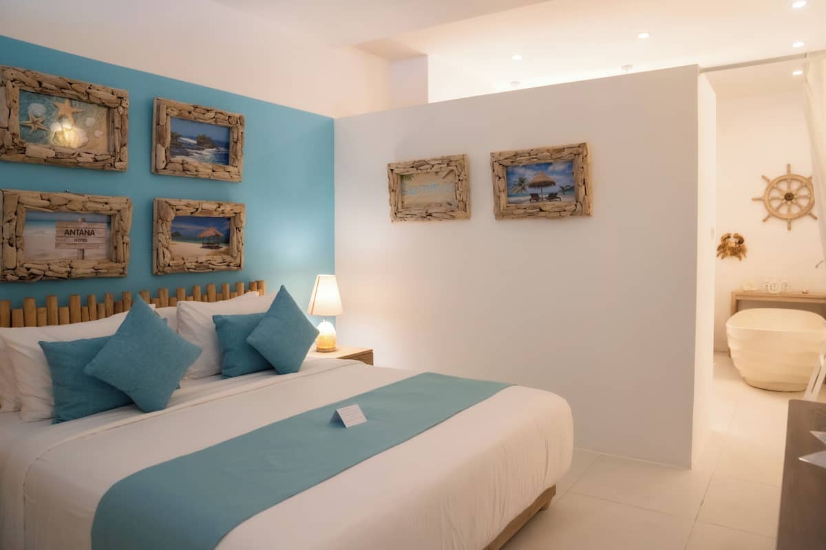 Een slaapkamer met een bed, een nachtkastje, een lamp en lijstjes met foto's aan de muur.