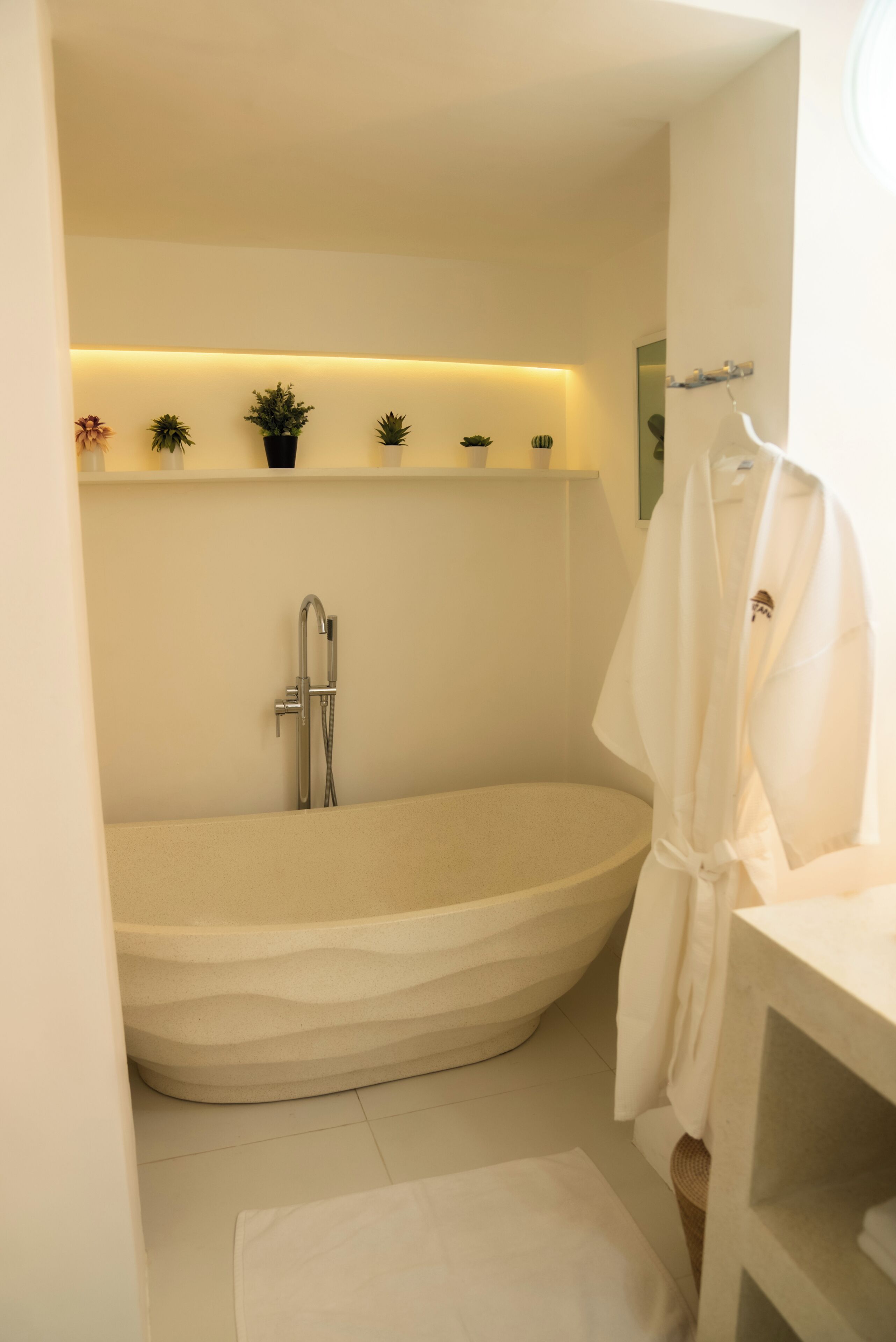 A modern bathroom with a freestanding bathtub, a white robe hanging on a rack, and a shelf with potted plants.