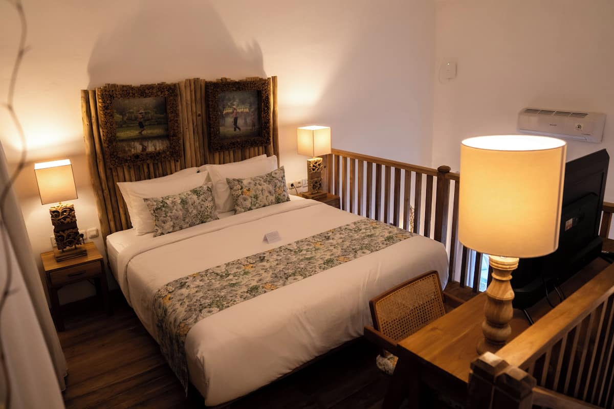 Een net opgemaakt bed met bloemenbeddengoed, een houten hoofdbord met ingelijste foto’s, bedlampen en een televisie op een houten dressoir.