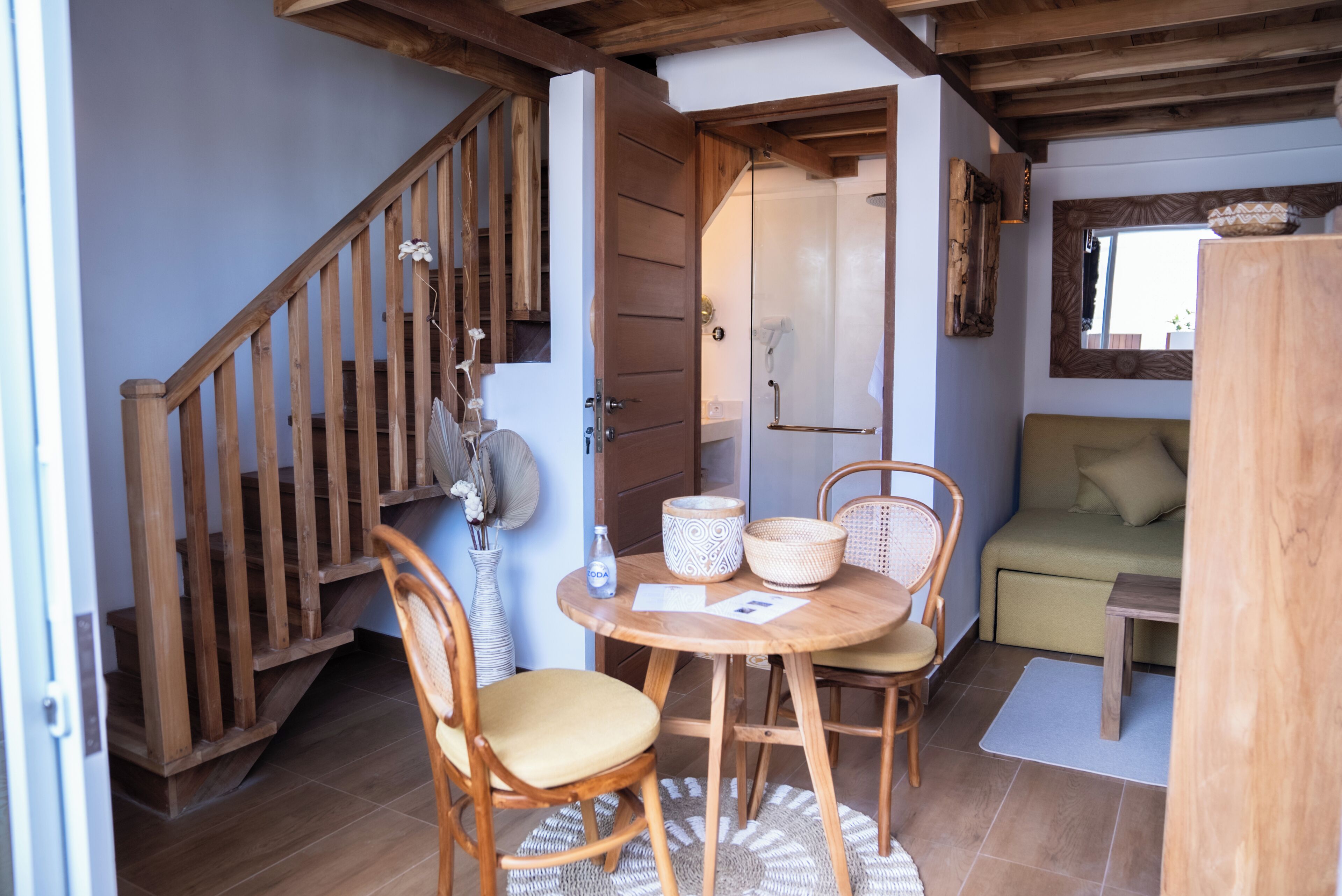 A cozy room with a wooden staircase, a round wooden table with chairs, a green sofa, and a small wooden table.