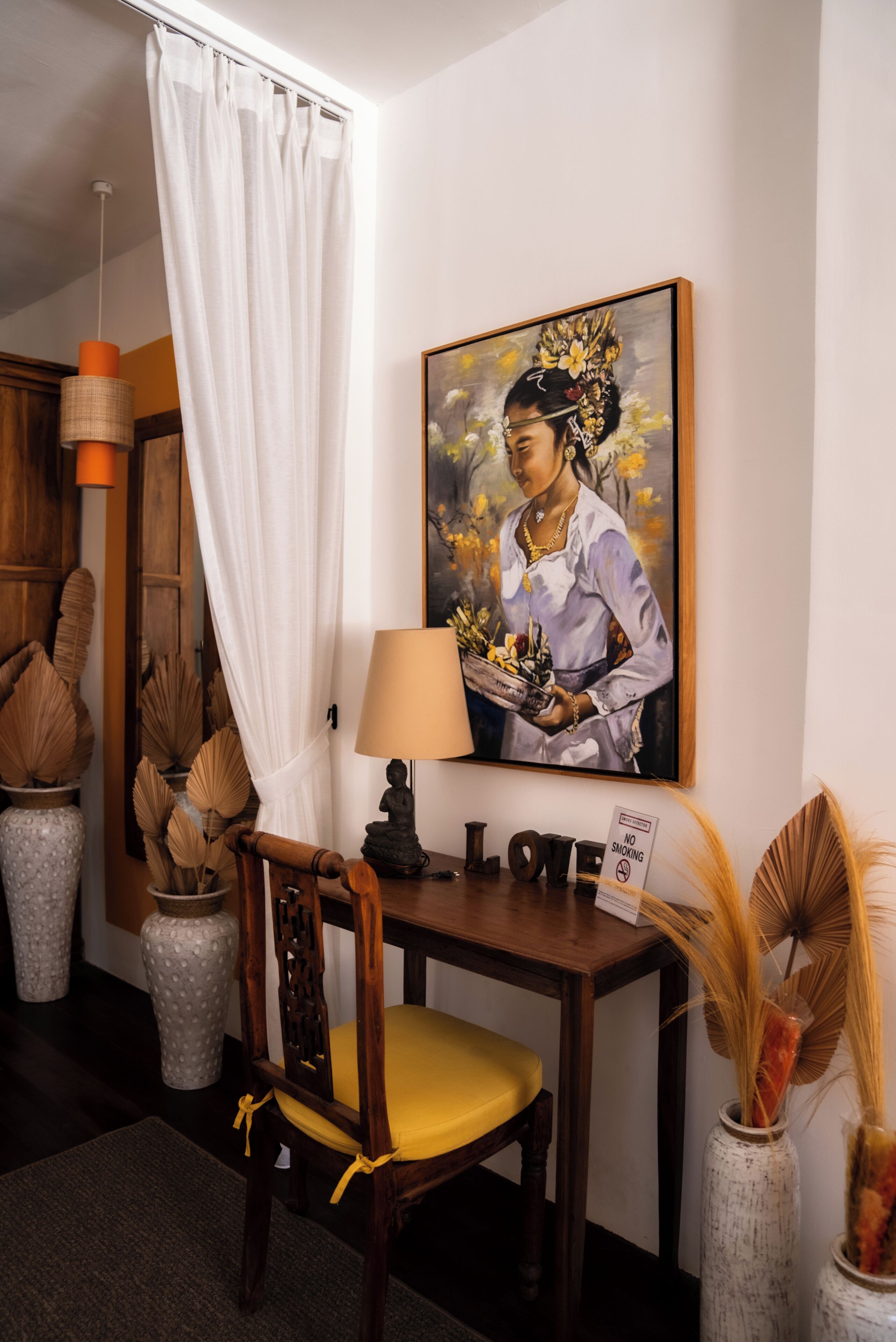A room with a wooden chair, a table with a lamp, a painting, and a 'No Smoking' sign.