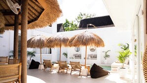 Un espace extérieur ensoleillé, aménagé avec des parasols en chaume, des meubles en osier et une piscine.